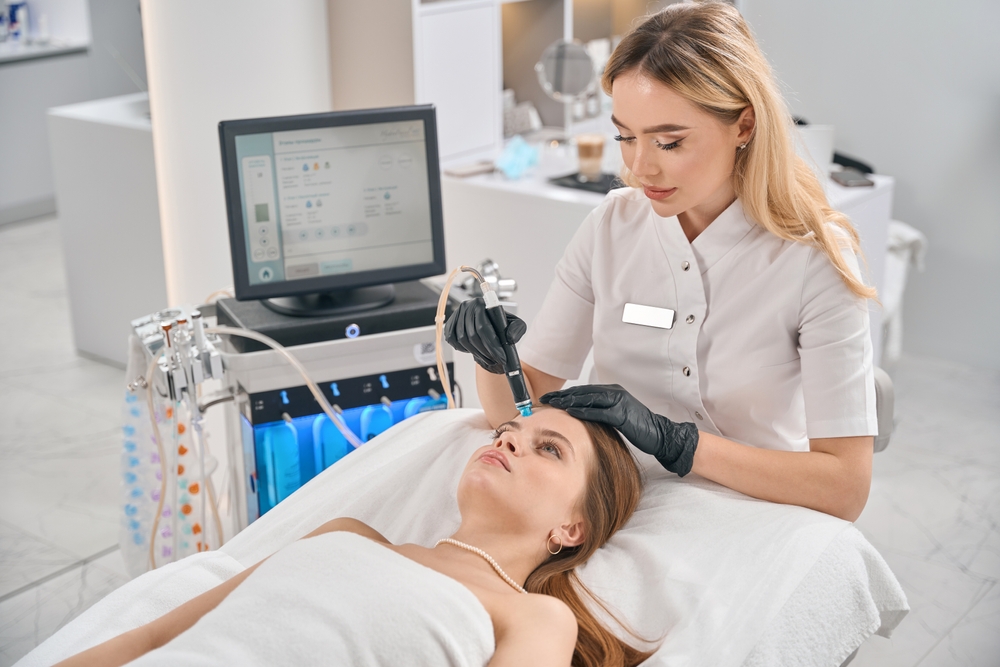 Kosmetička provádí hydrafacial ošetření obličeje ženy ležící na lehátku.